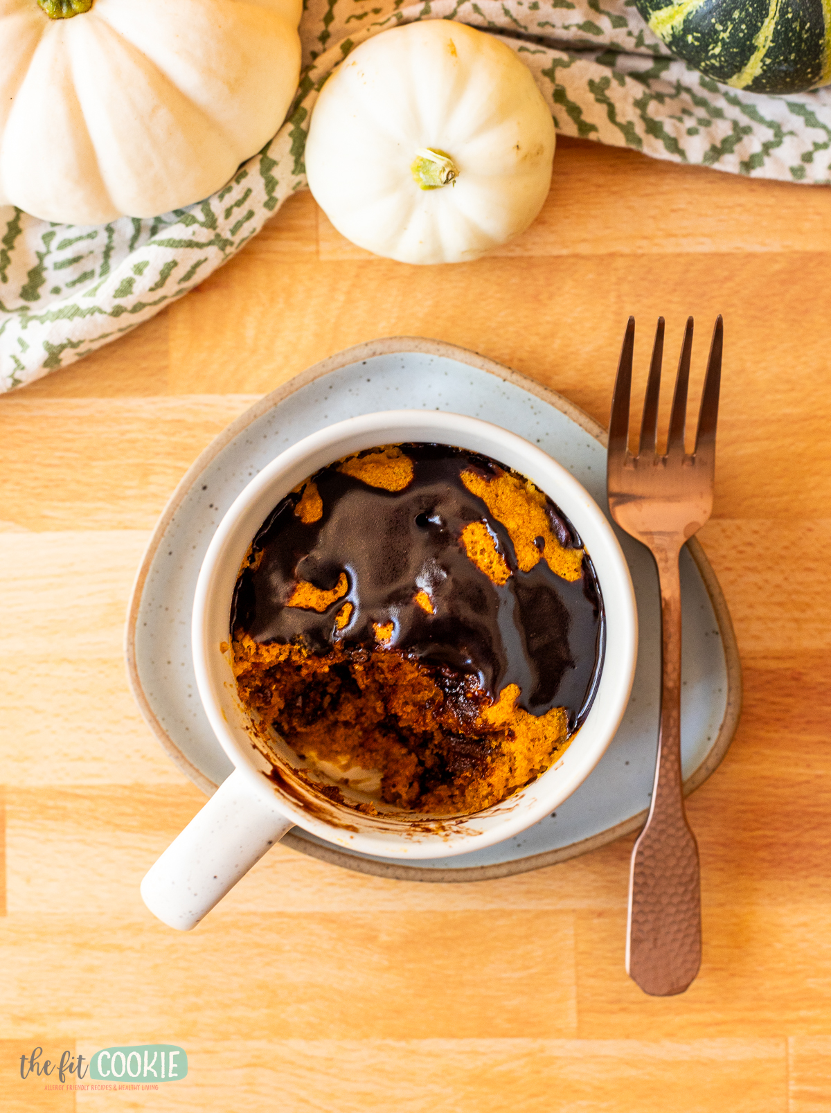 A pumpkin mug cake with a fork next to it on a wood butcher block.