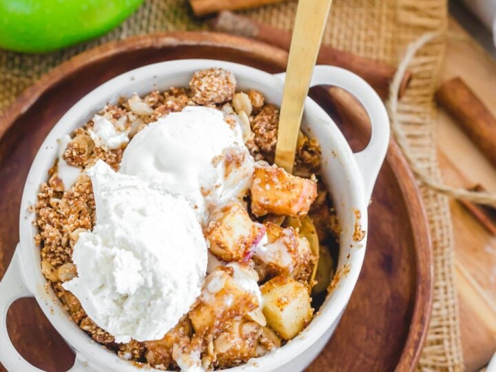 A bowl of apple crisp with ice cream and apples.