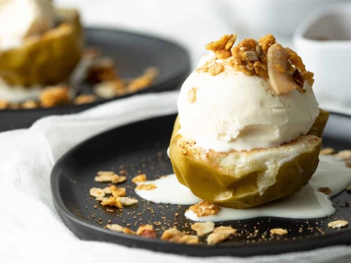Two black plates with ice cream and granola on them.