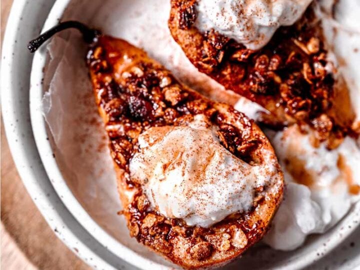 Two pears topped with granola and whipped cream.