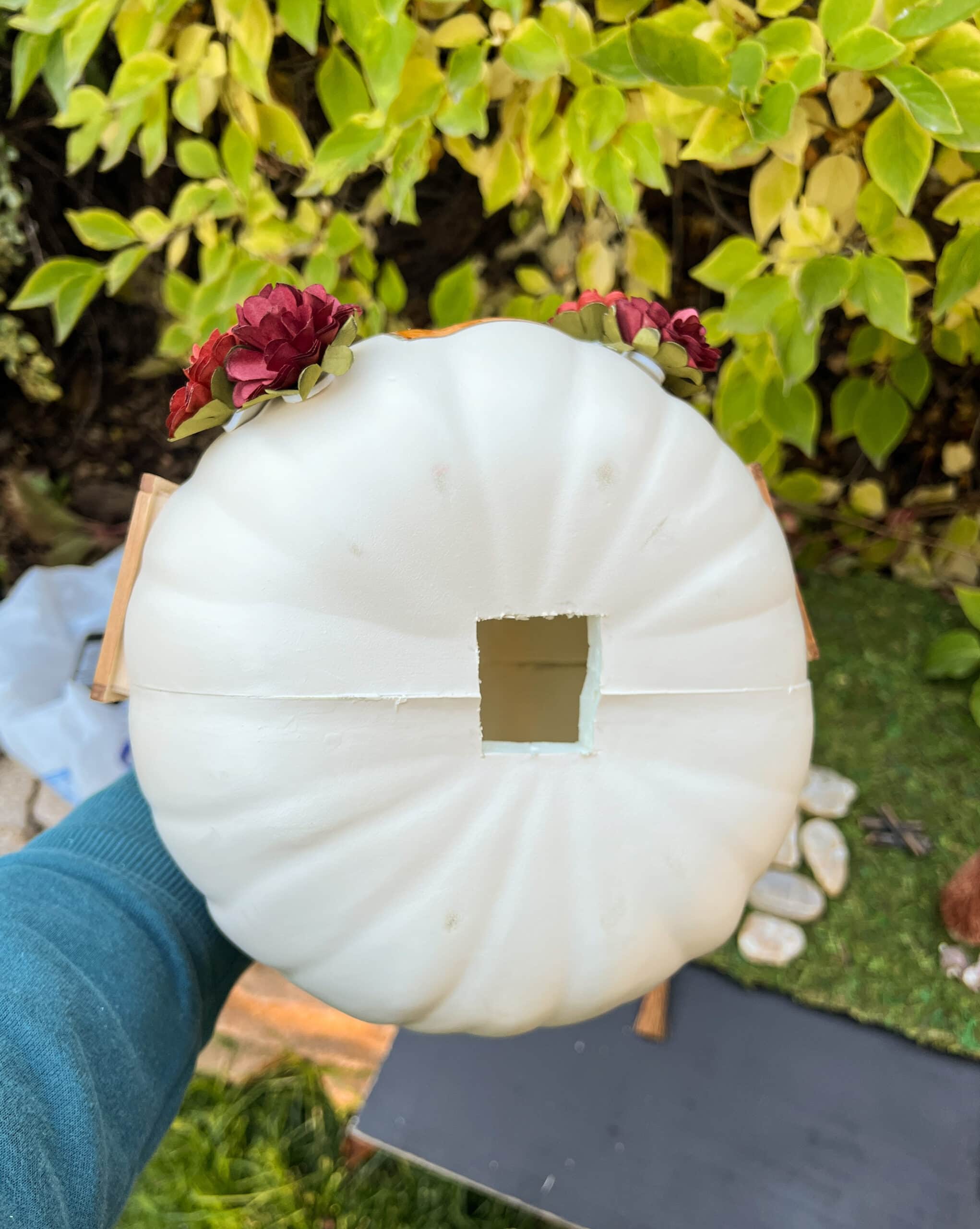 A person holding a white craft pumpkin with a square hole in it. 