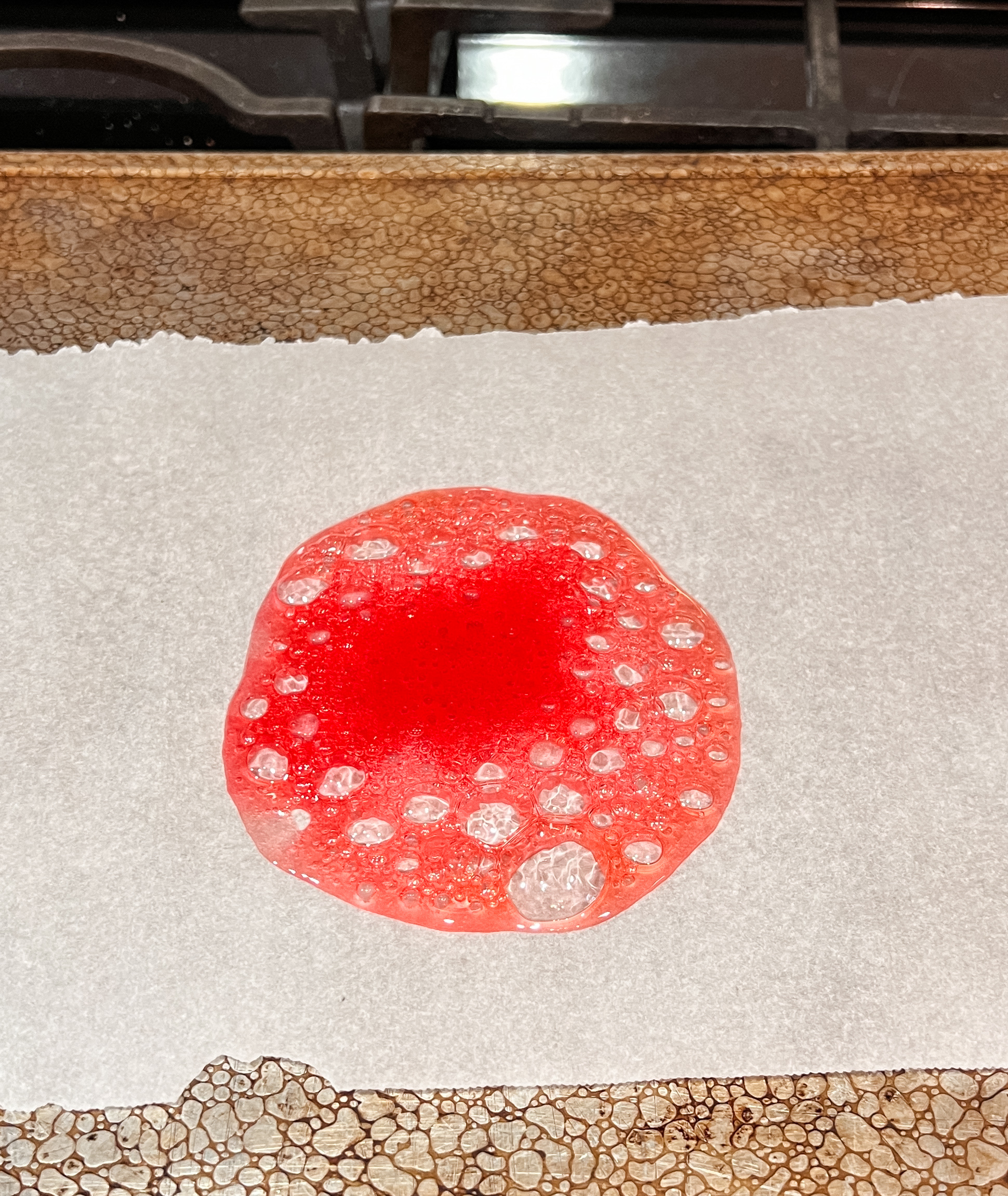 A piece of melted red candy with bubbles in it on parchment paper.