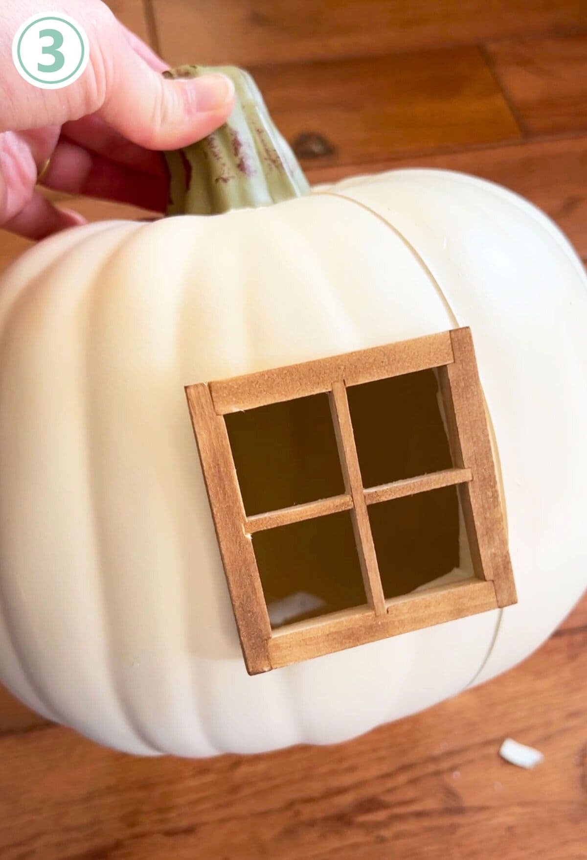 A person is holding a white pumpkin with a window on it.