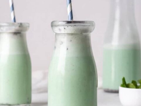 A green smoothie in a glass with a straw and chocolate chips.