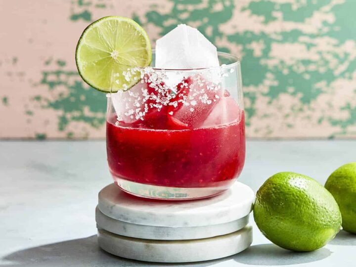 A margarita in a glass with limes and ice.