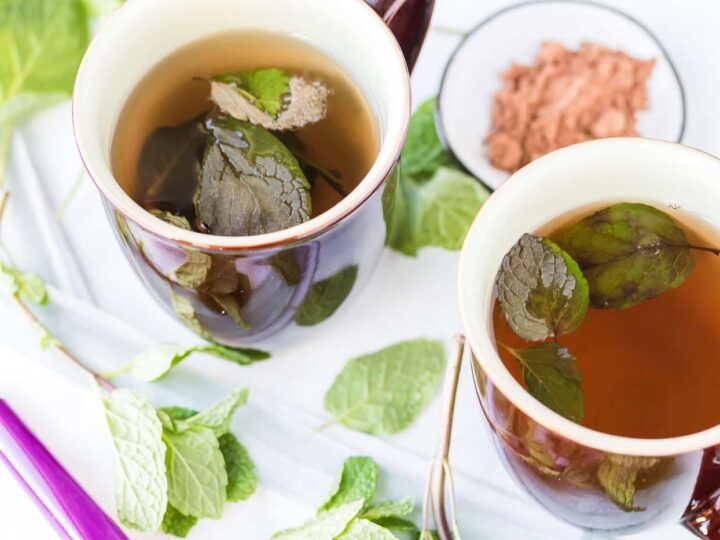 Two mugs of tea with mint leaves in them.