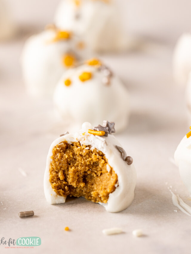 White chocolate pumpkin truffles with a bite taken out of them.