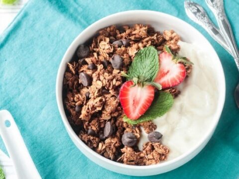 A bowl of chocolate granola with strawberries and mint.