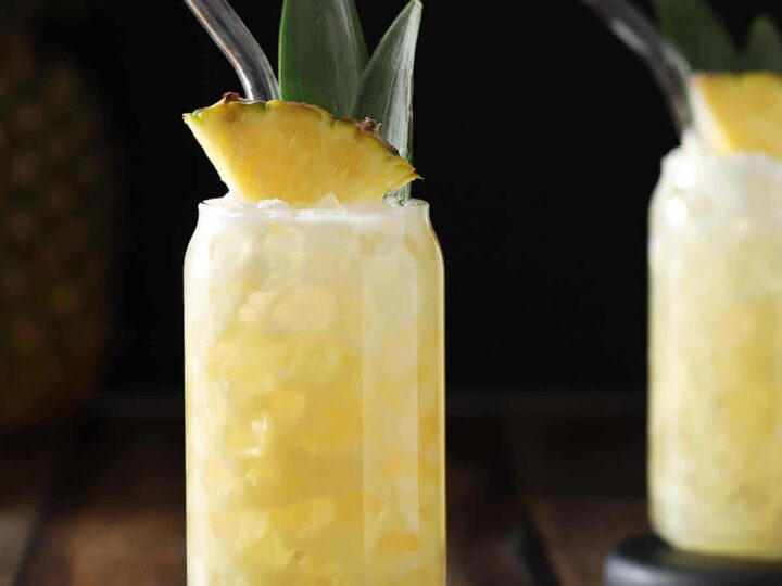 A pineapple rum cocktail with a straw on a wooden table.