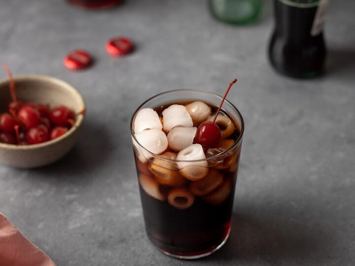 A glass of coca cola with cherries and ice.