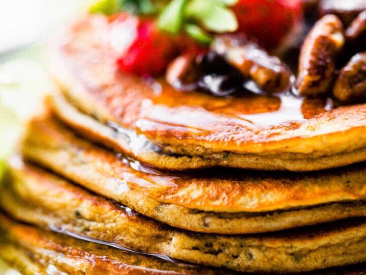A stack of pancakes with strawberries and pecans on a plate.
