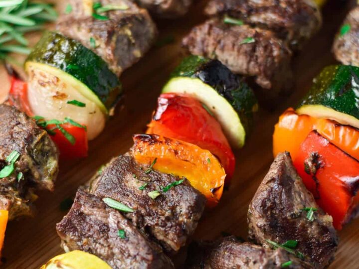 Beef skewers with vegetables and herbs on a wooden cutting board.