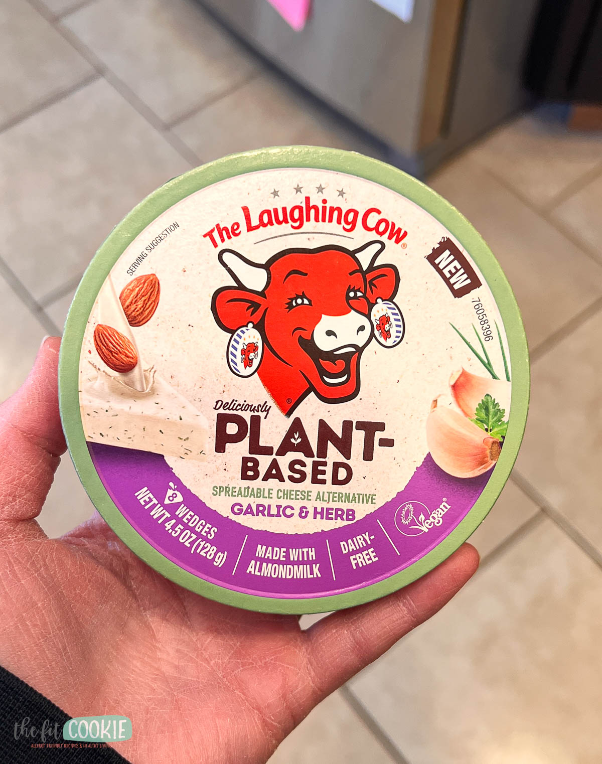 A hand holds a container of The Laughing Cow plant-based spreadable cheese.