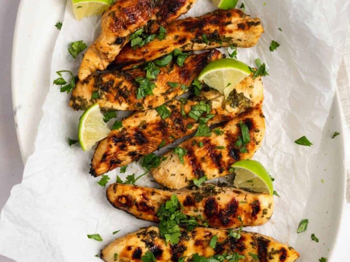 Grilled chicken on a white plate with lime wedges.