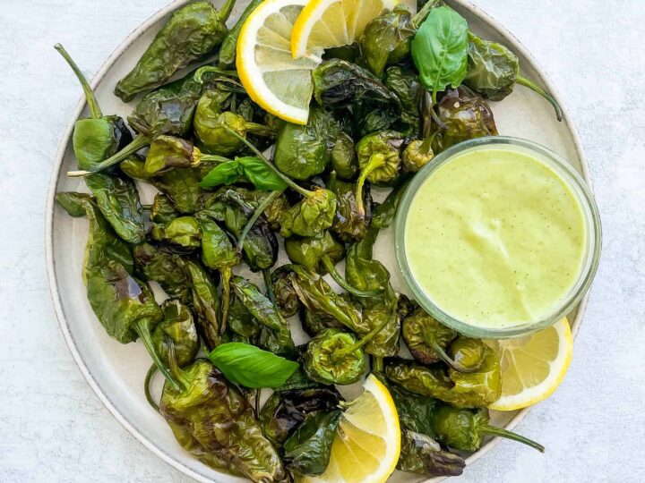 A plate with green peppers and lemon wedges on it.