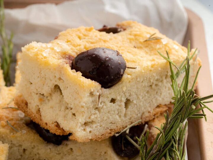 A piece of bread with olives and sprigs of rosemary.