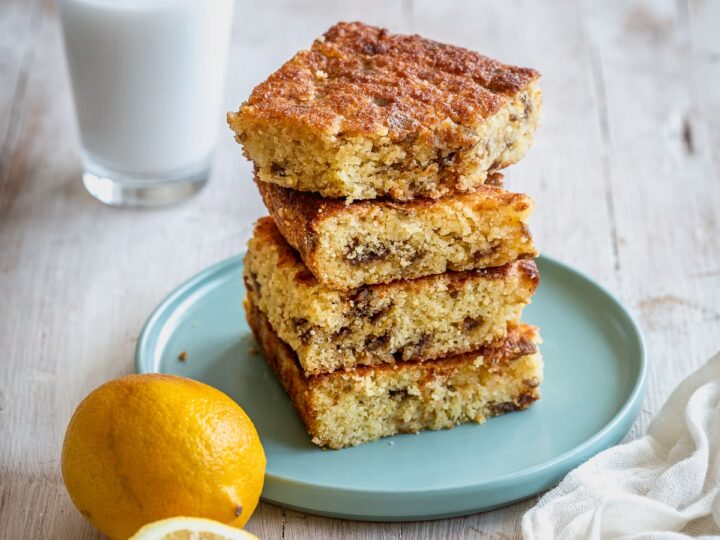 A stack of lemon bars on a plate with a glass of milk.