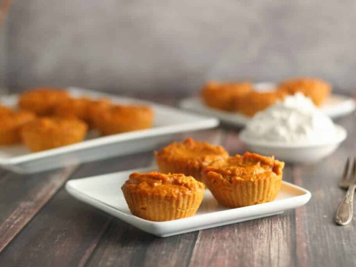 Pumpkin cupcakes on white plates with whipped cream.