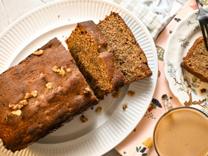 A slice of banana bread on a plate next to a cup of coffee.