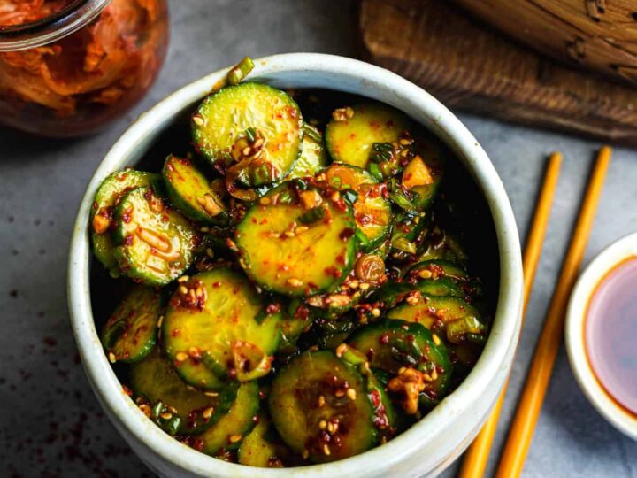 A bowl of asian cucumbers in a bowl with chopsticks.