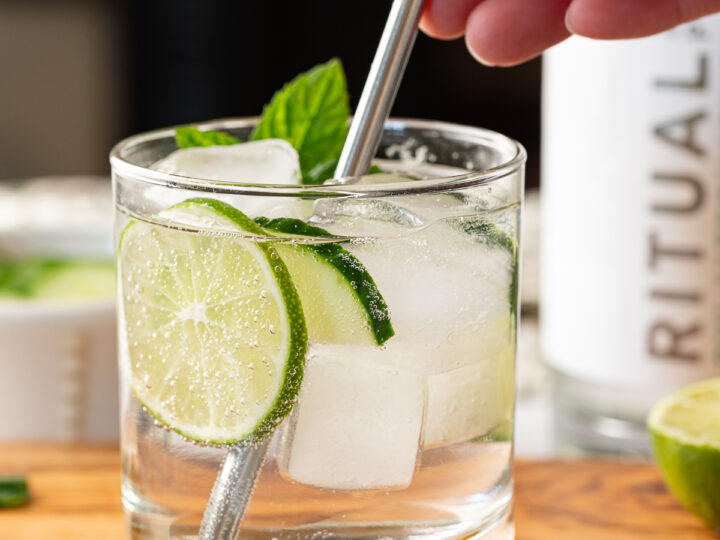 Someone stirring a metal straw in a glass of non-alcoholic gin and tonic.