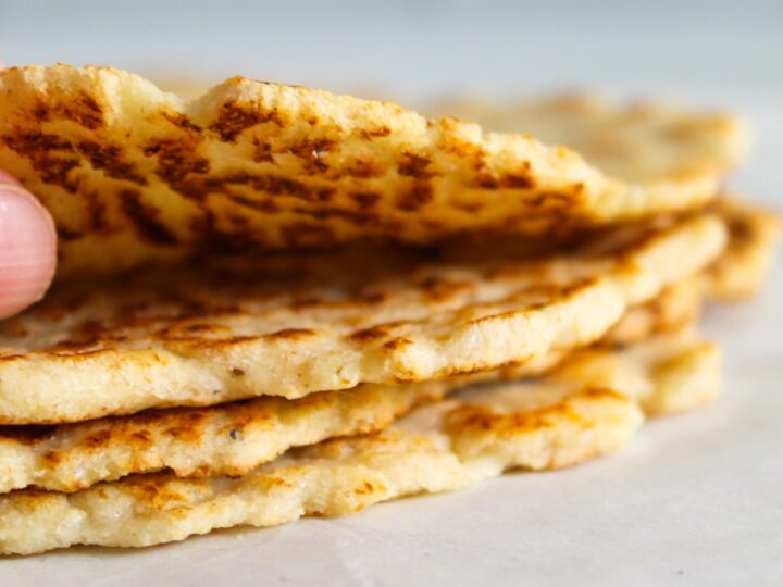 A person is holding a stack of flatbreads.