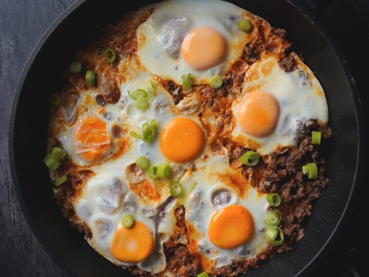 A frying pan with eggs and meat in it.
