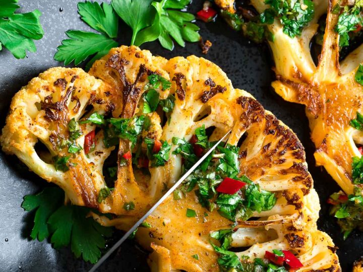 Two roasted cauliflowers on a plate with parsley and parmesan.