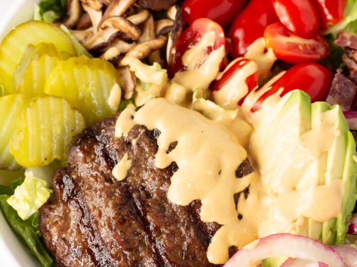 A salad with burgers, tomatoes and avocados.