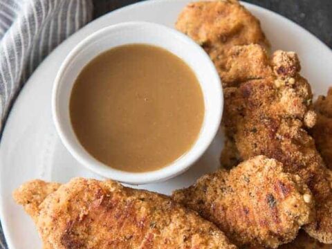 Fried chicken fingers with dipping sauce on a plate.