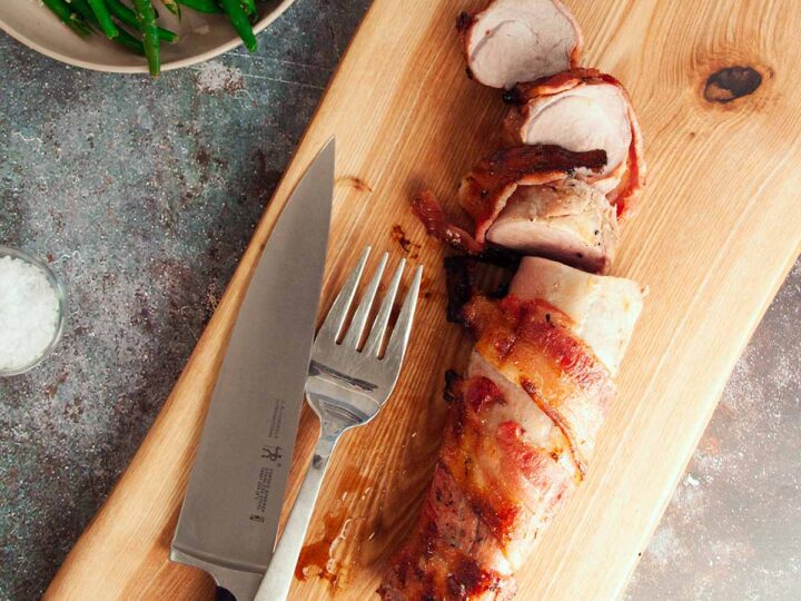A knife and fork on a wooden cutting board.