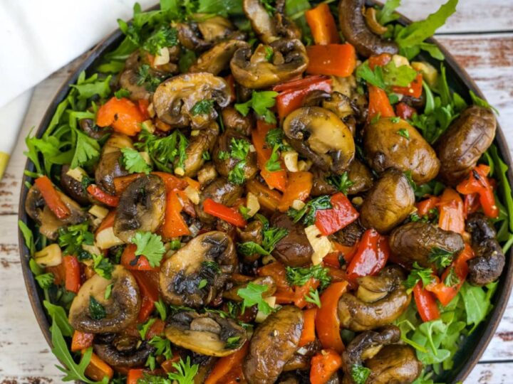 A bowl with mushrooms, peppers and arugula.
