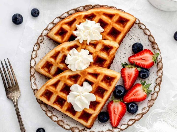 Waffles with whipped cream and berries on a plate.