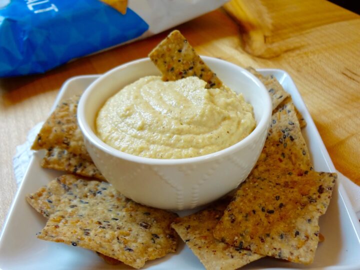 A bowl of dairy-free hummus on a plate with crackers, perfect for low carb recipes.
