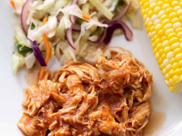 Bbq pulled pork on a plate with coleslaw and corn on the cob.