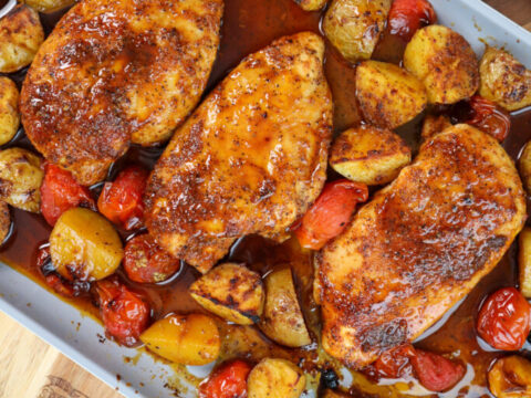 Chicken breasts and potatoes on a baking sheet.