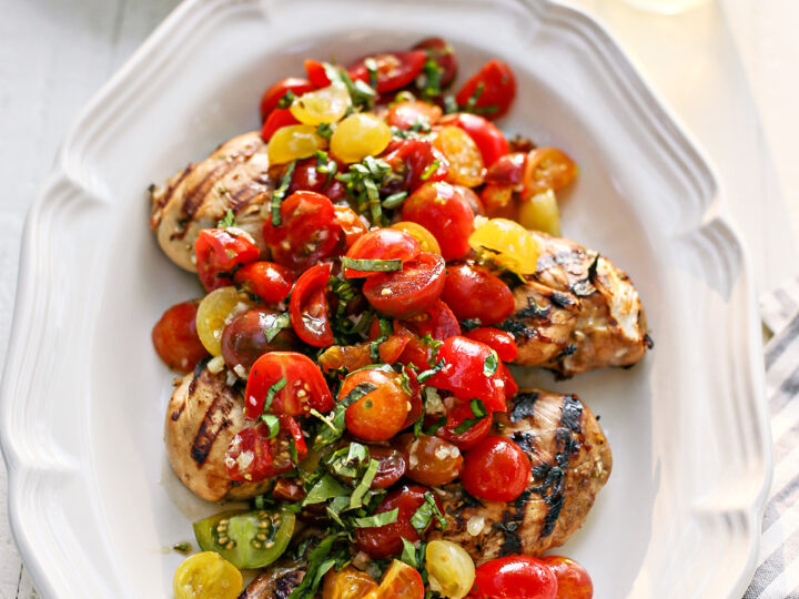 A white plate with chicken breast and tomatoes on it.