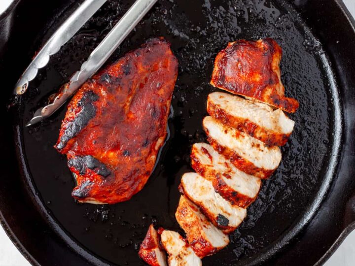 Grilled chicken breasts in a skillet with a fork.