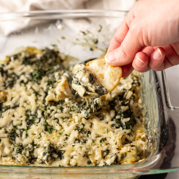 A person dipping a chip into a dish of spinach artichoke dip.