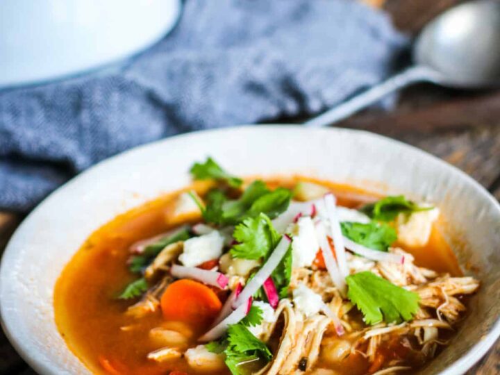A bowl of mexican chicken soup on a wooden table.