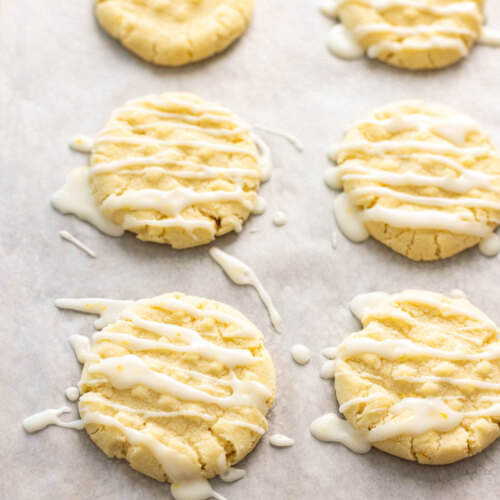 A baking sheet pan with parchment paper on it with lemon cookies drizzled with icing.