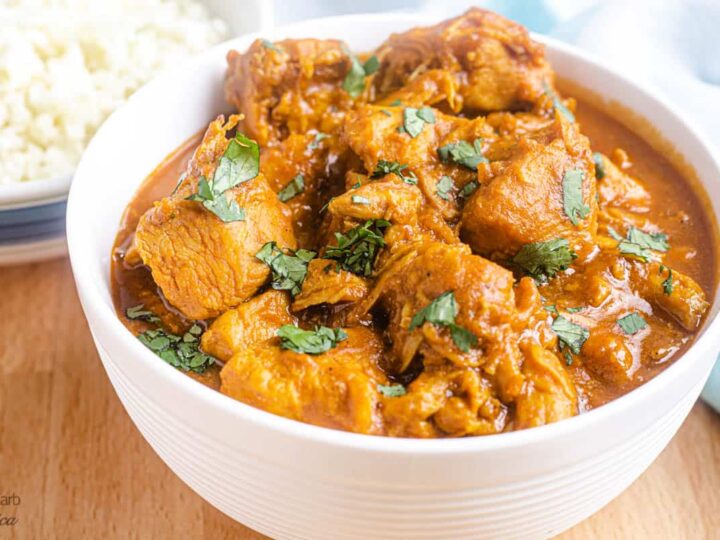 Chicken curry in a white bowl on a wooden table.