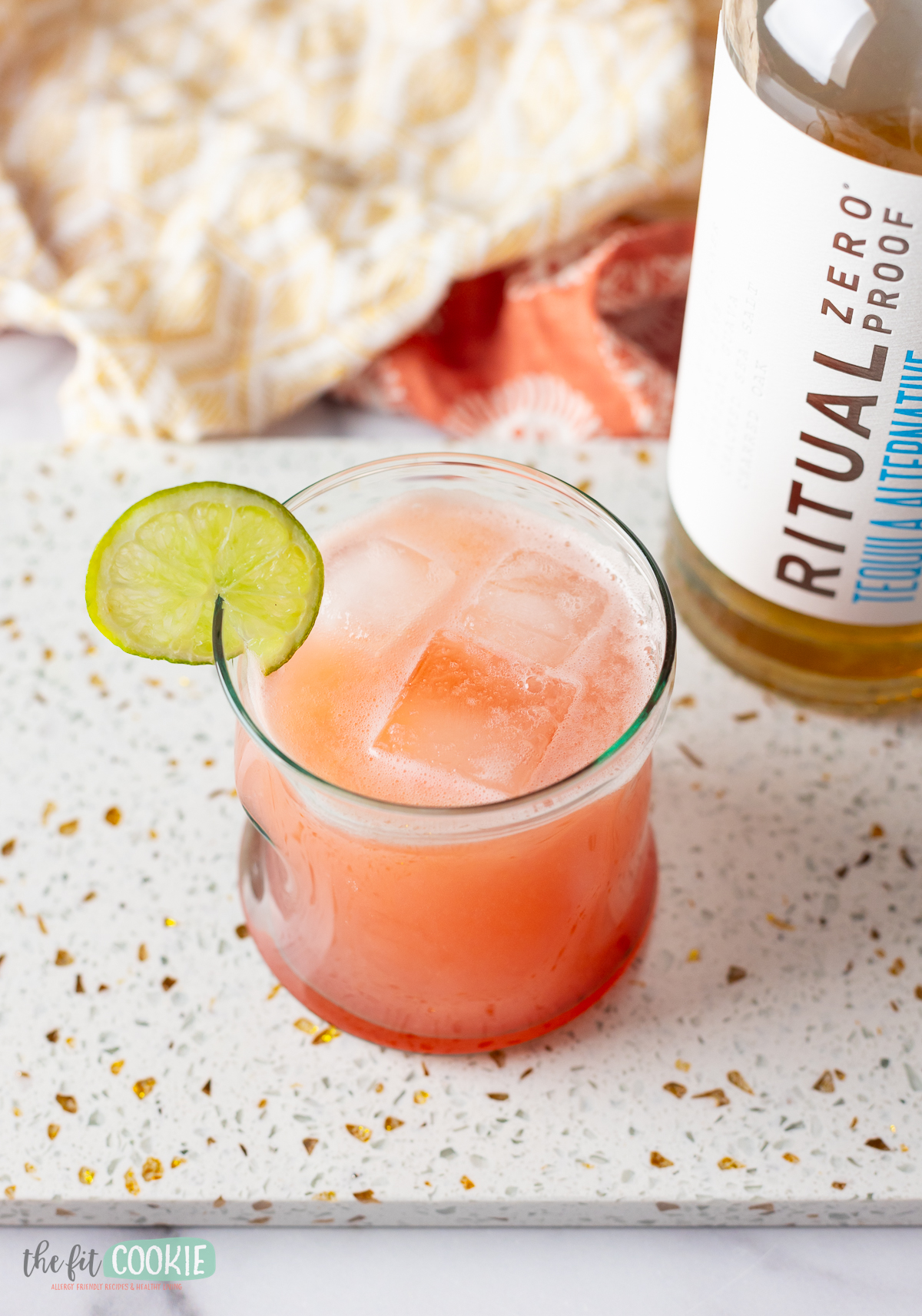 A strawberry paloma mocktail with a lime and a bottle next to it.
