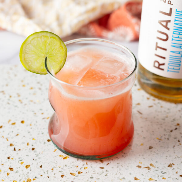 A glass with a lime on it next to a bottle of rum, perfect for making a refreshing Paloma cocktail.