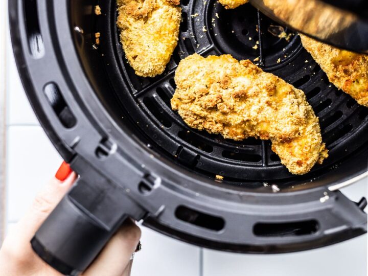 A person holding a piece of chicken in an air fryer.