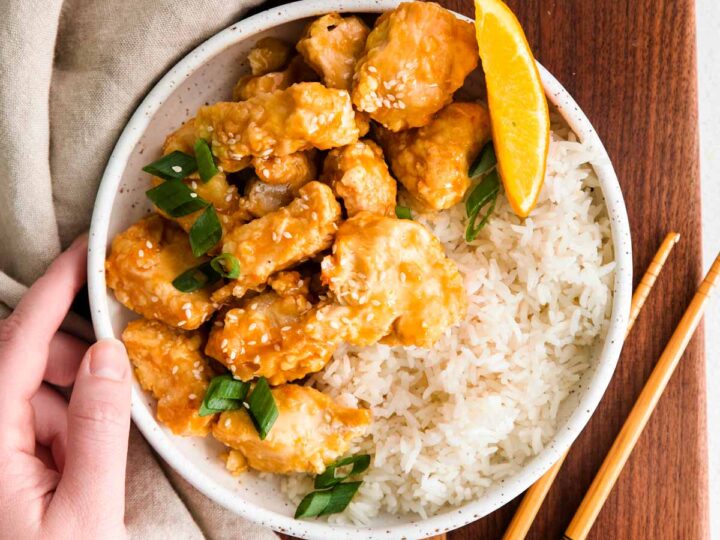 A bowl of orange chicken with rice and chopsticks.