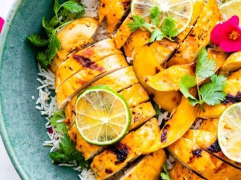 Grilled chicken on a plate with rice and lemon wedges.