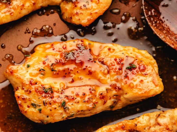 Chicken breasts in a pan with sauce and a spoon.