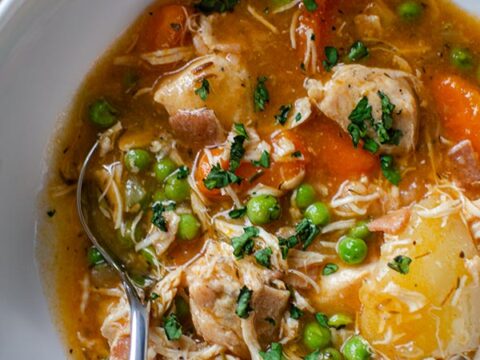 A bowl of chicken soup with carrots and peas.