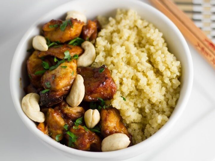 A white bowl with chicken, rice and cashews.